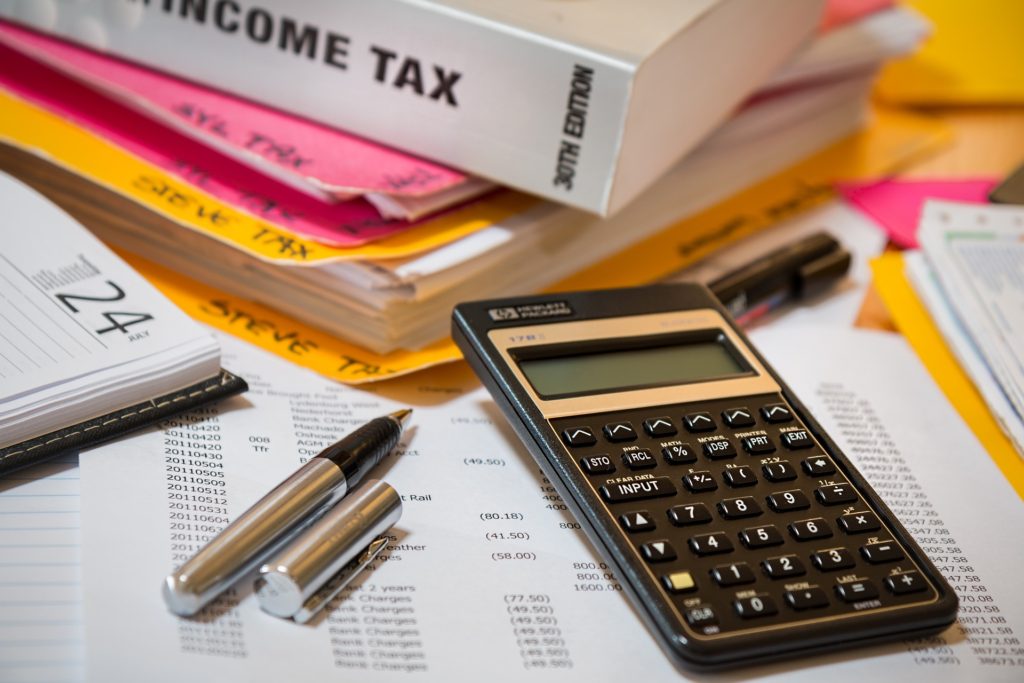 A photograph of a book titled "income tax" amidst a pile of papers, a calculator, and some pens on a desk.